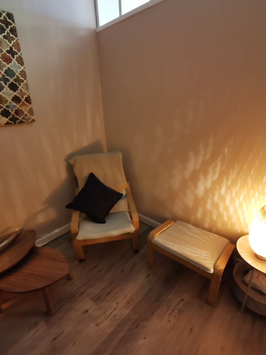 A wooden armchair and footstool in warm lamp light
