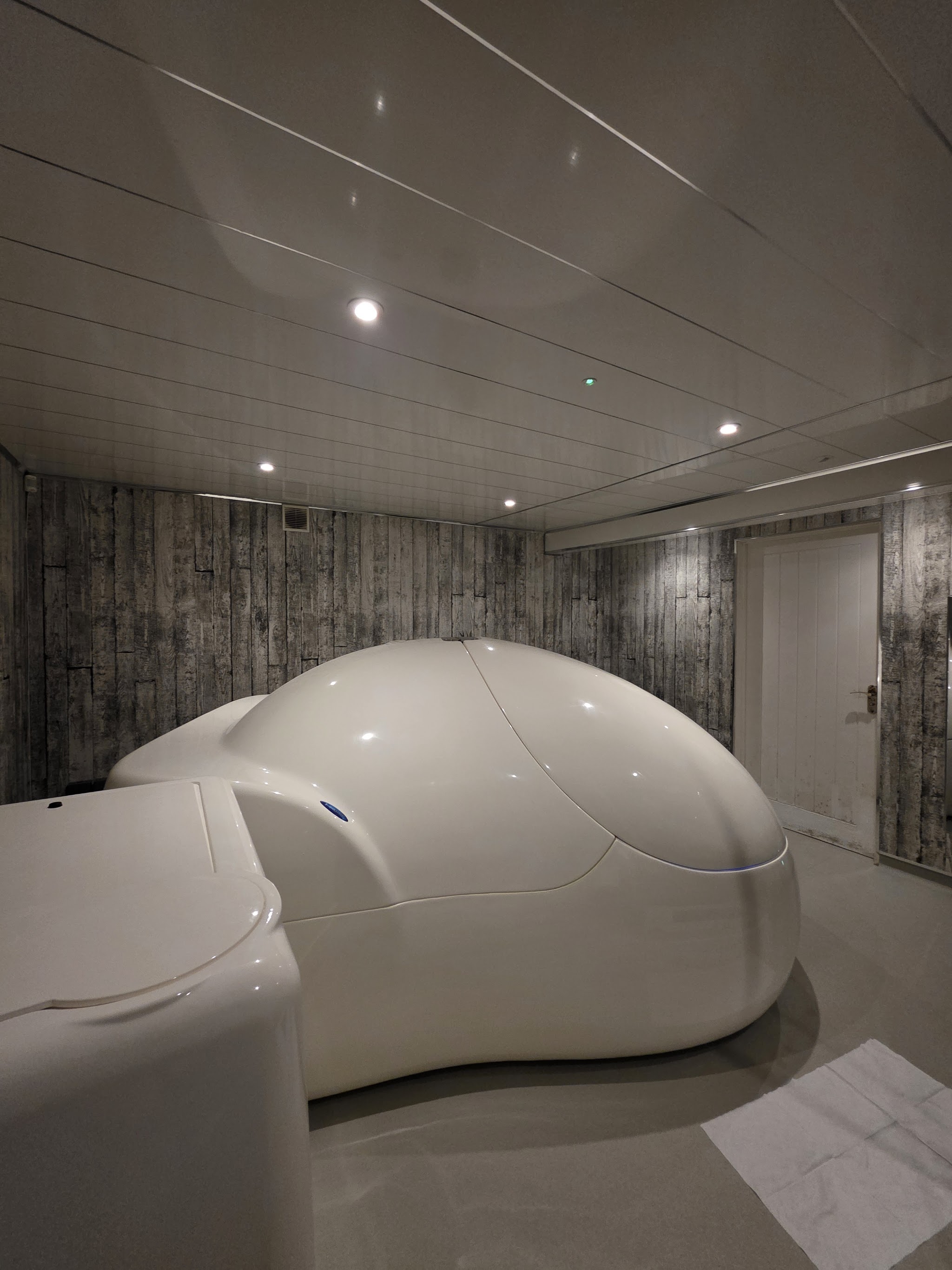 A closed white float pod in a float room with wood effect walls